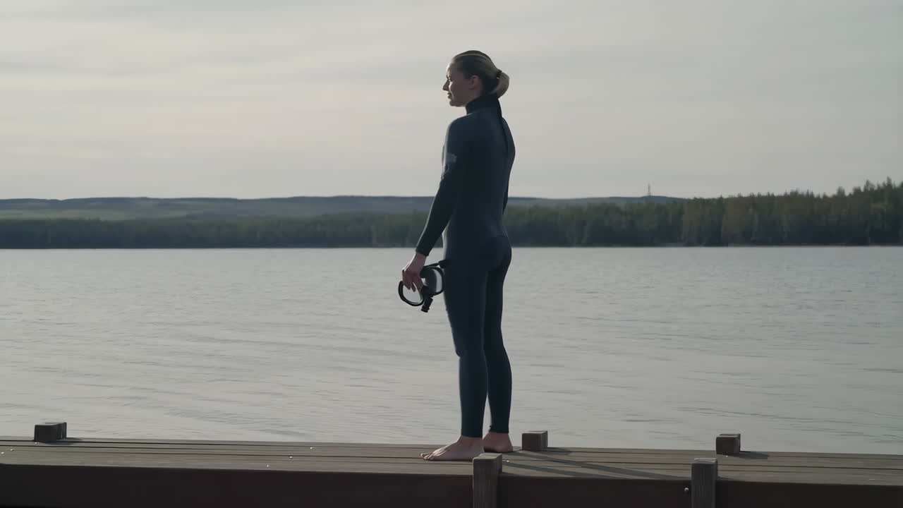 Woman in Wetsuit Holding Diving Mask on a Dock by a Lake