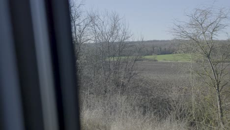 view from train window over green fields and woods, springtime and peaceful vibe
