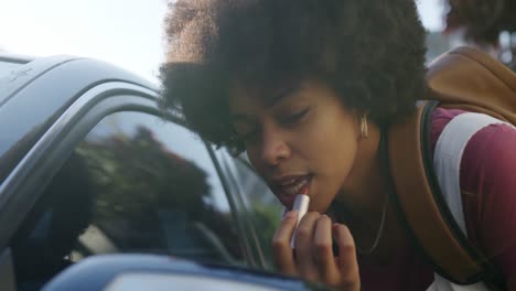 mixed race woman putting lipstick in rear-view mirror