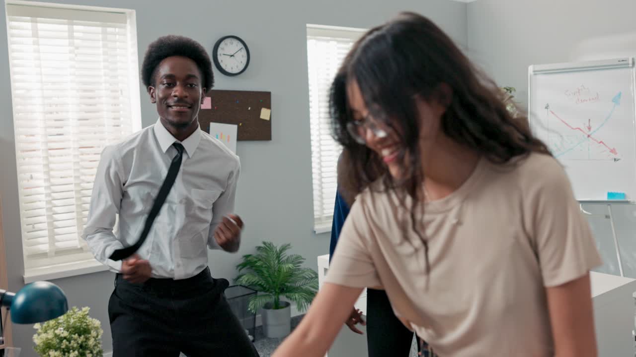 Dança no trabalho, no escritório, durante uma pausa ou festa da empresa; duas moças e um homem de camisa e gravata dançam juntos, se divertem, riem, sorriem, aliviando o estresse, com música tocando do computador