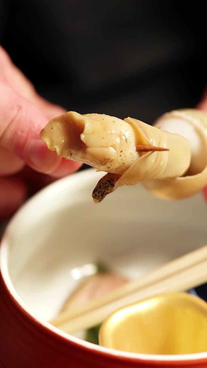 Primo piano macro di mani che estraggono frutti di mare cotti da un guscio usando uno stuzzicadenti di legno