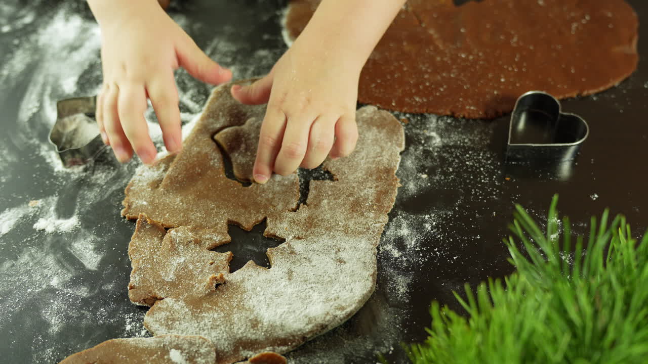 Child baking cookies, hands cutting dough with festive shapes on floured surface