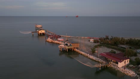 Vista-Aérea-De-Cabañas-De-Pesca-A-Orillas-Del-Estuario-Al-Atardecer,-Máquina-De-Pesca-Italiana,-Llamada-&quot-4