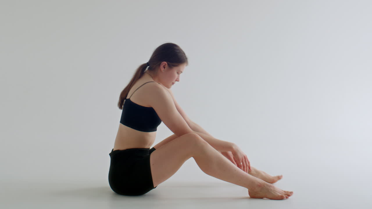 Yogini che esegue la posizione di equilibrio sulle braccia Tittibhasana in uno studio bianco