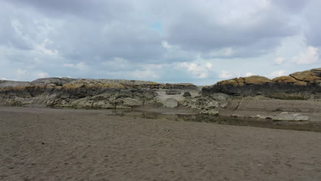 Tracking-shot-of-along-the-flat-sand-showing-some-small-rock-cliffs-on-the-uk-coast-line