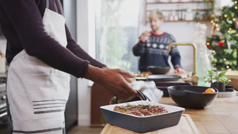 gay male couple in kitchen cooking dinner on christmas day taking vegetarian nut roast out of oven