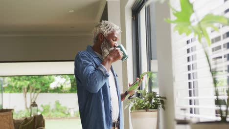 Video-of-african-american-senior-man-drinking-coffee-and-using-tablet