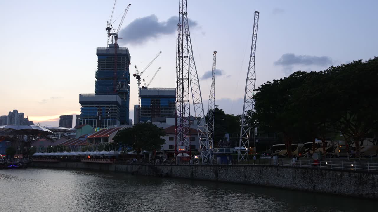 Camera pans along Singapore riverfront at dusk, revealing skyline, cranes, and waterfront promenade