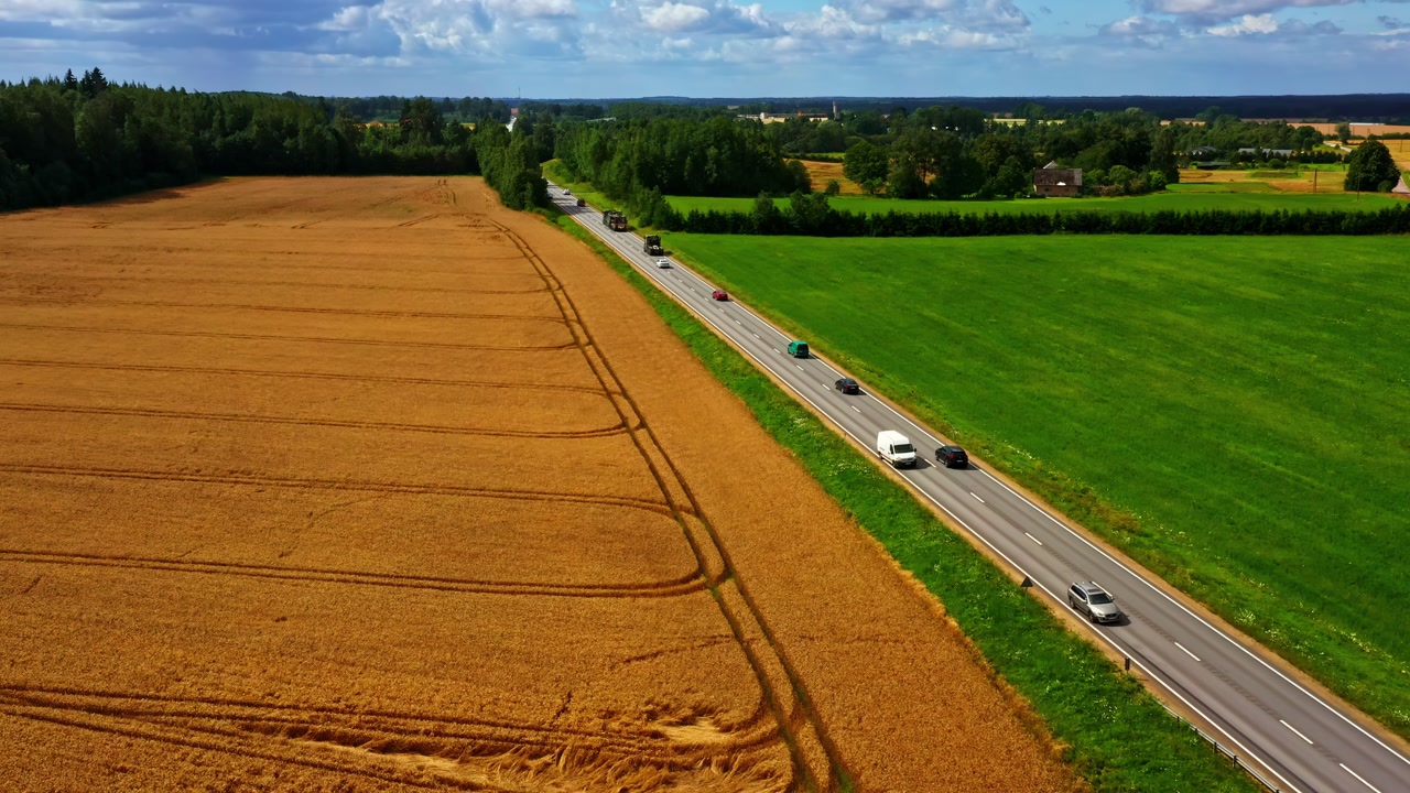 Highway road cutting through rural landscape of fields and forests with traffic seen from above