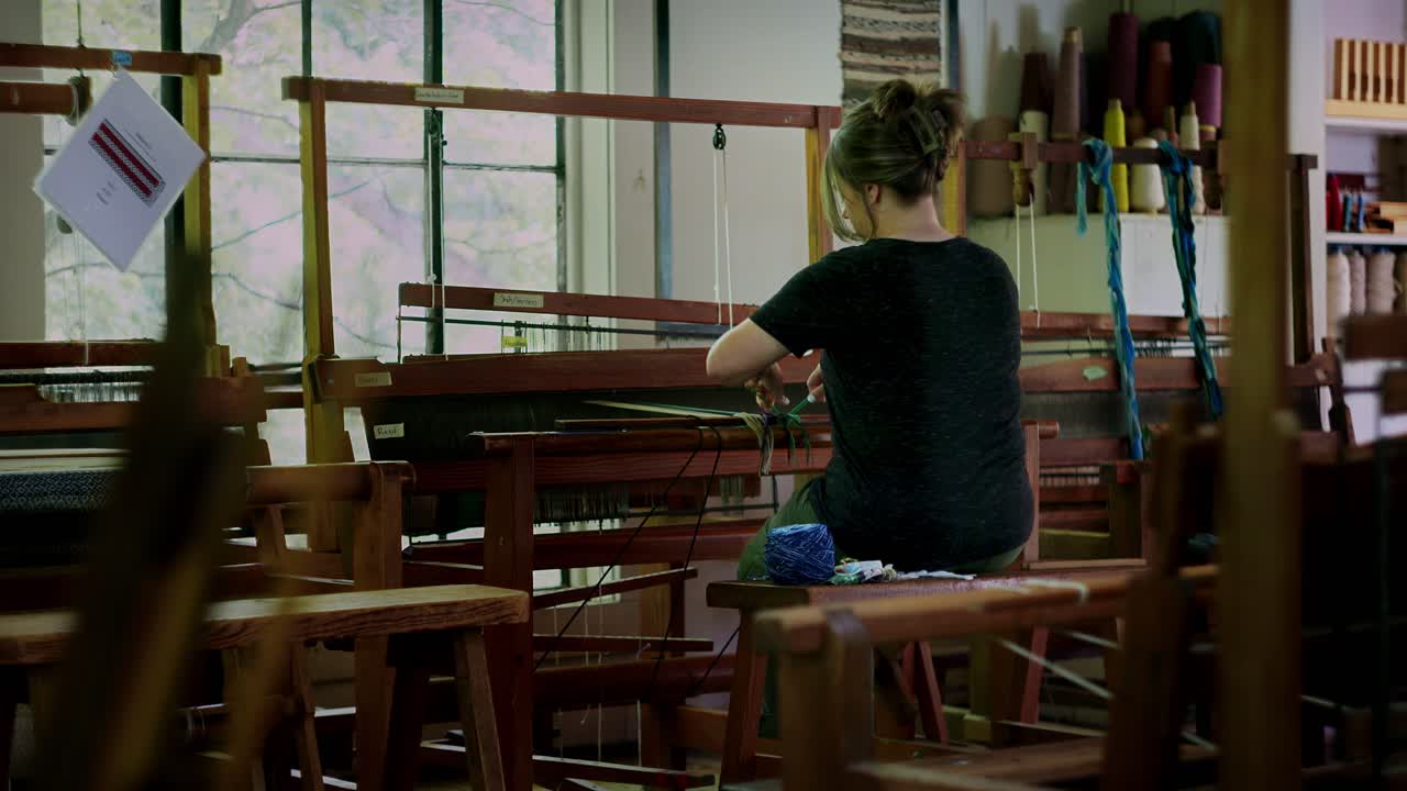 Woman sits at sewing loom working with hands to prepare and tie knots, cinematic