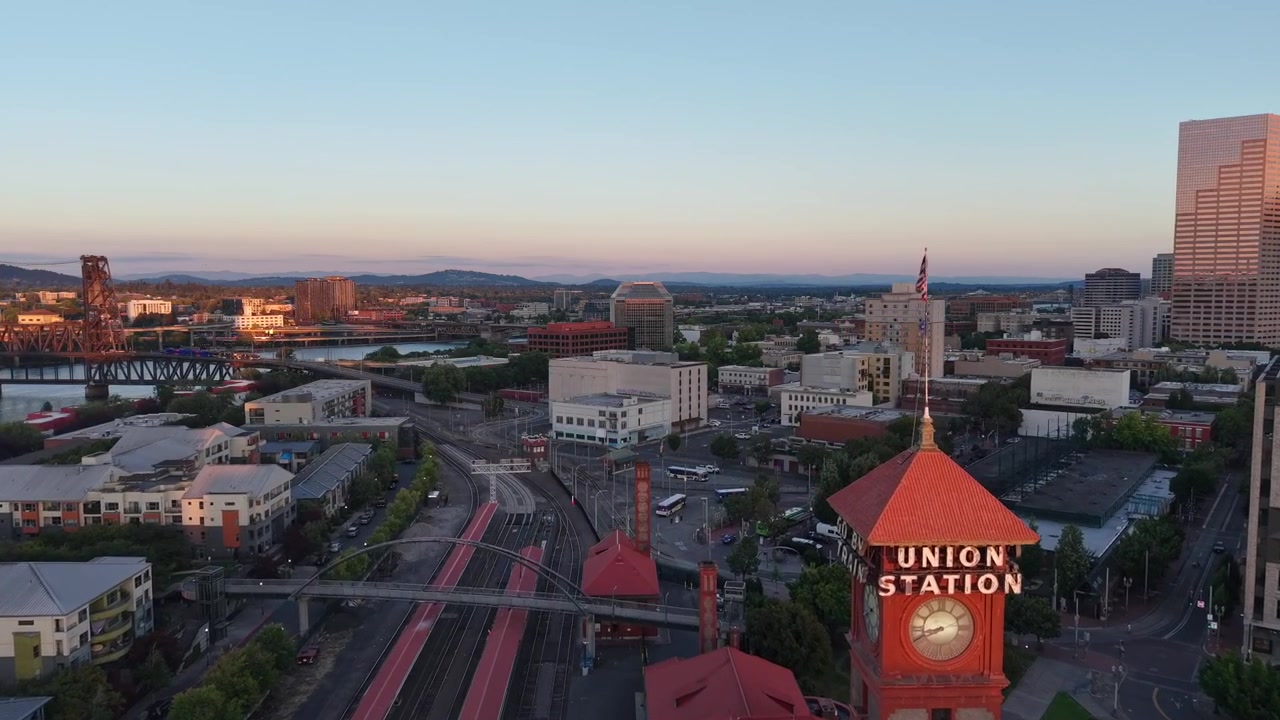 Una ripresa aerea fluida con drone del Pearl District di Portland, Oregon, e dello skyline del centro al tramonto, con l'iconica torre dell'orologio della Union Station, il vicino scalo ferroviario e il ponte Fremont in una calda serata