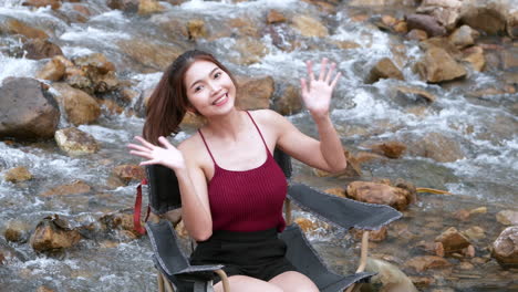 Mujer-Asiática-De-Rojo-Sentada-En-Una-Silla-Con-Grandes-Rocas-Y-Agua-Salpicando-Lentamente-Para-Relajarse-Y-Ser-Feliz-En-Las-Vacaciones-De-Verano