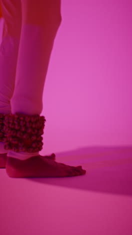 vertical video close up of feet with bells of female kathak dancer performing dance wearing traditional indian dress against purple background 2