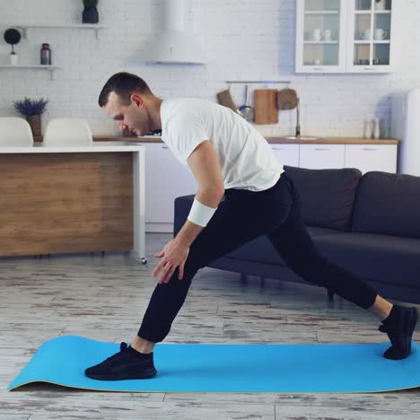 young man doing fitness at home. man in t-shirt and pants is doing exercises on mat at home in his spacious kitchen