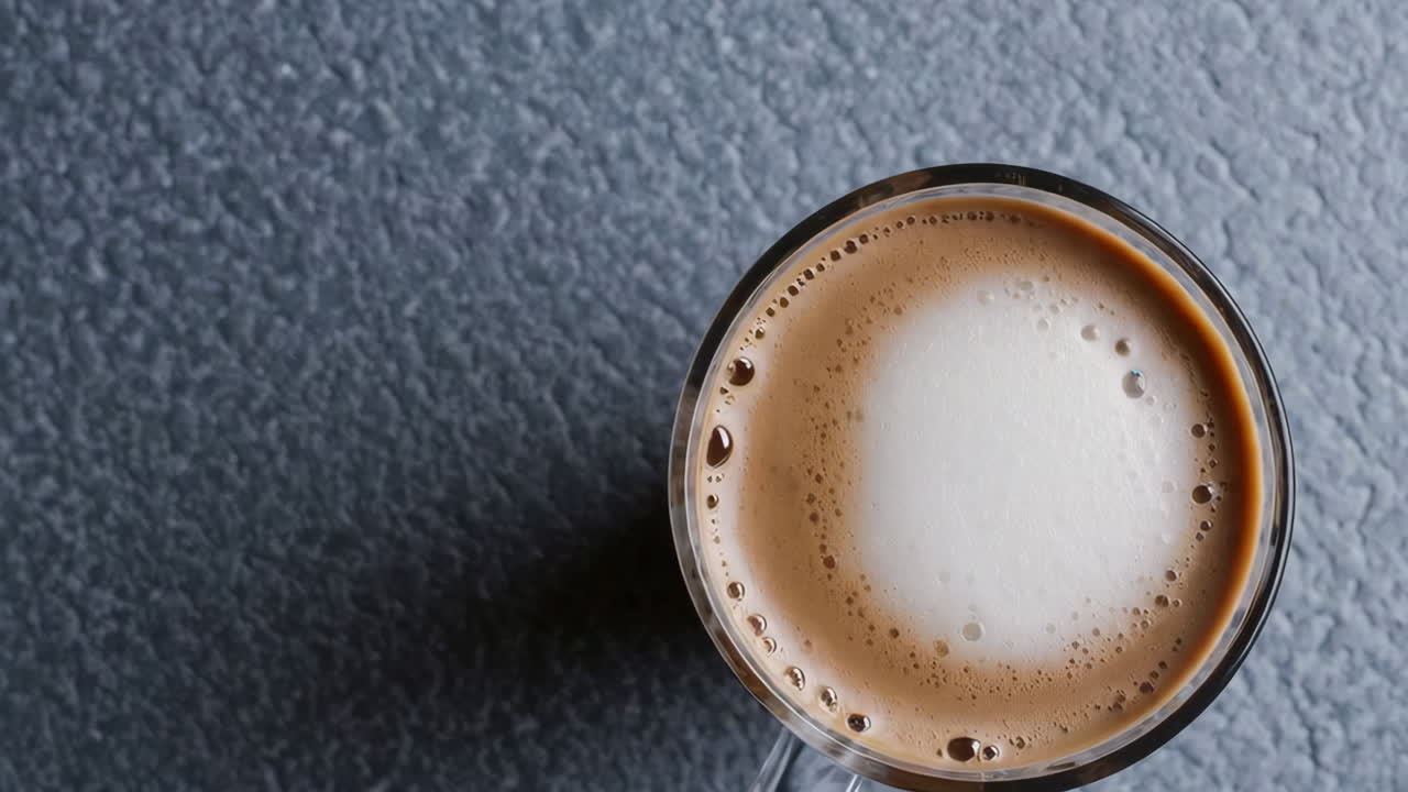 Overhead view of a coffee or latte with frothy foam on a dark textured surface