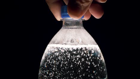 a bottle of carbonated water is unscrewed by hand on a black background