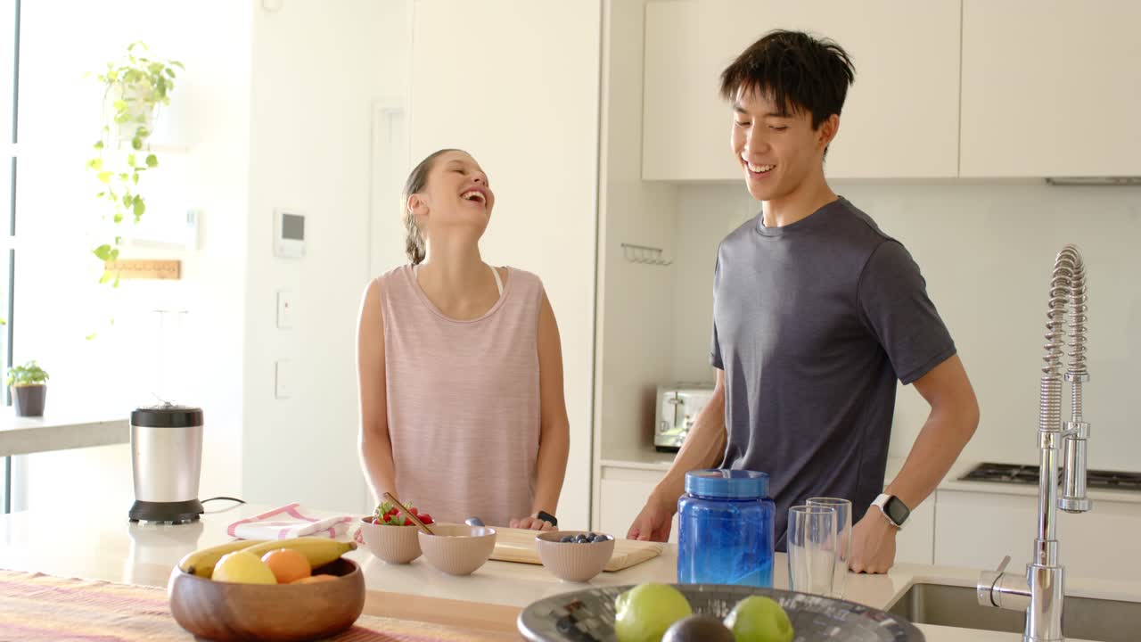 キッチンアイランドでスナックを準備するカップル。女性が話し始め、分け合うためのボウルを並べている。