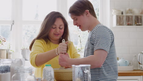 una pareja joven con síndrome de down mezcla ingredientes para una receta de pastel que están horneando en la cocina en casa.
