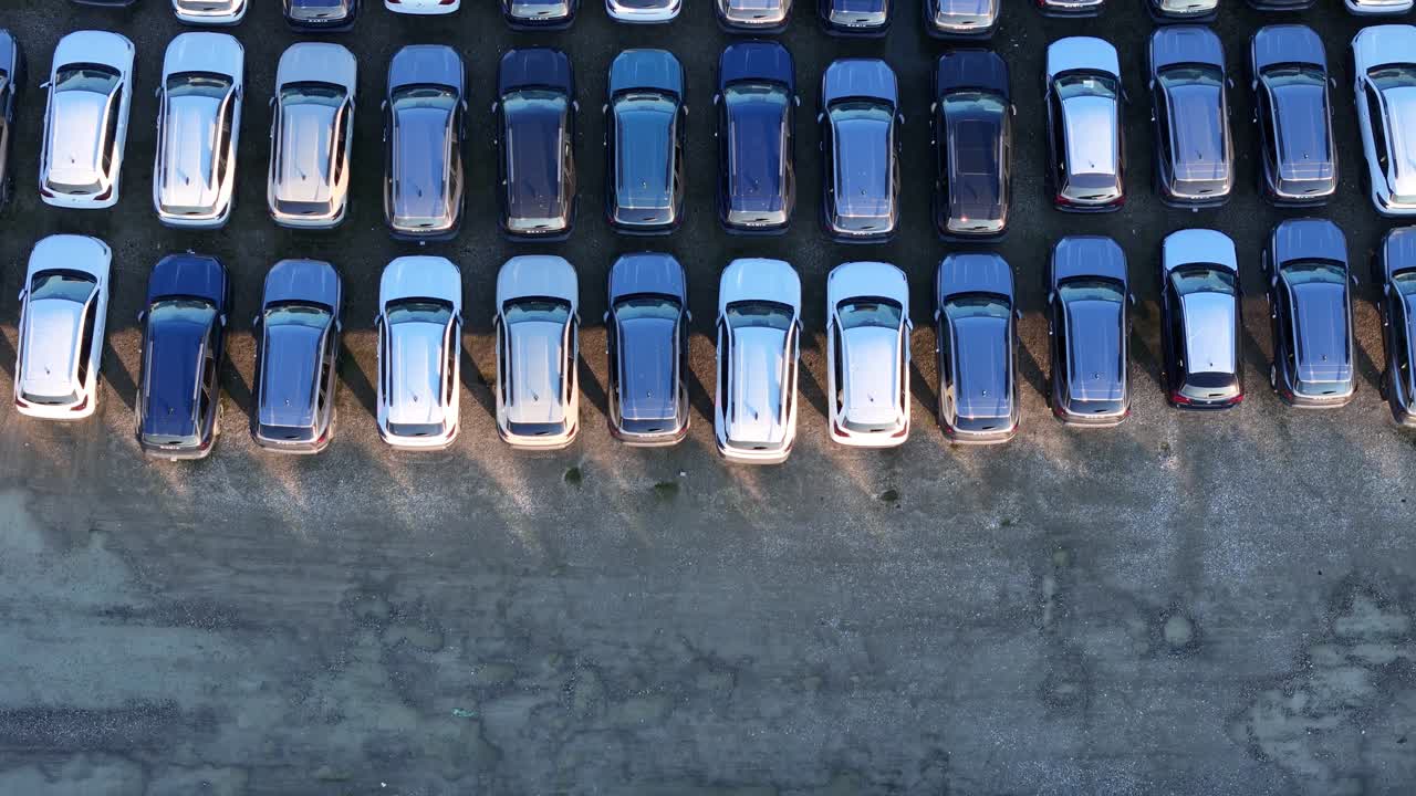 Luftfoto af rækker af importerede personbiler, der er parkeret på en stor logistikplads, der viser organiserede opbevaringsmønstre for køretøjer og adgangsveje, der bruges til transport.