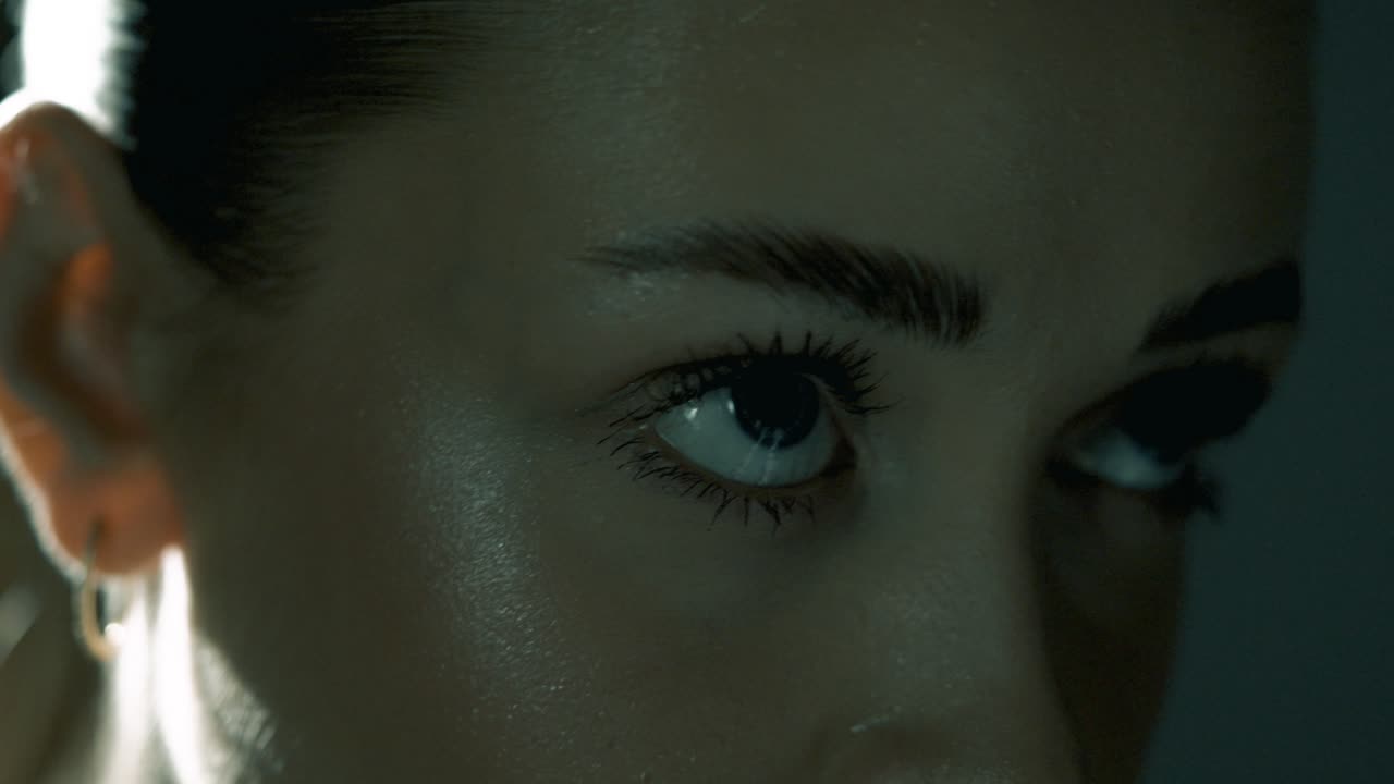 Smooth push-in toward a woman’s eyes from a slight profile angle as she cycles intensely, eyes locked forward in deep concentration. Soft cinematic light enhances her focus and facial tension