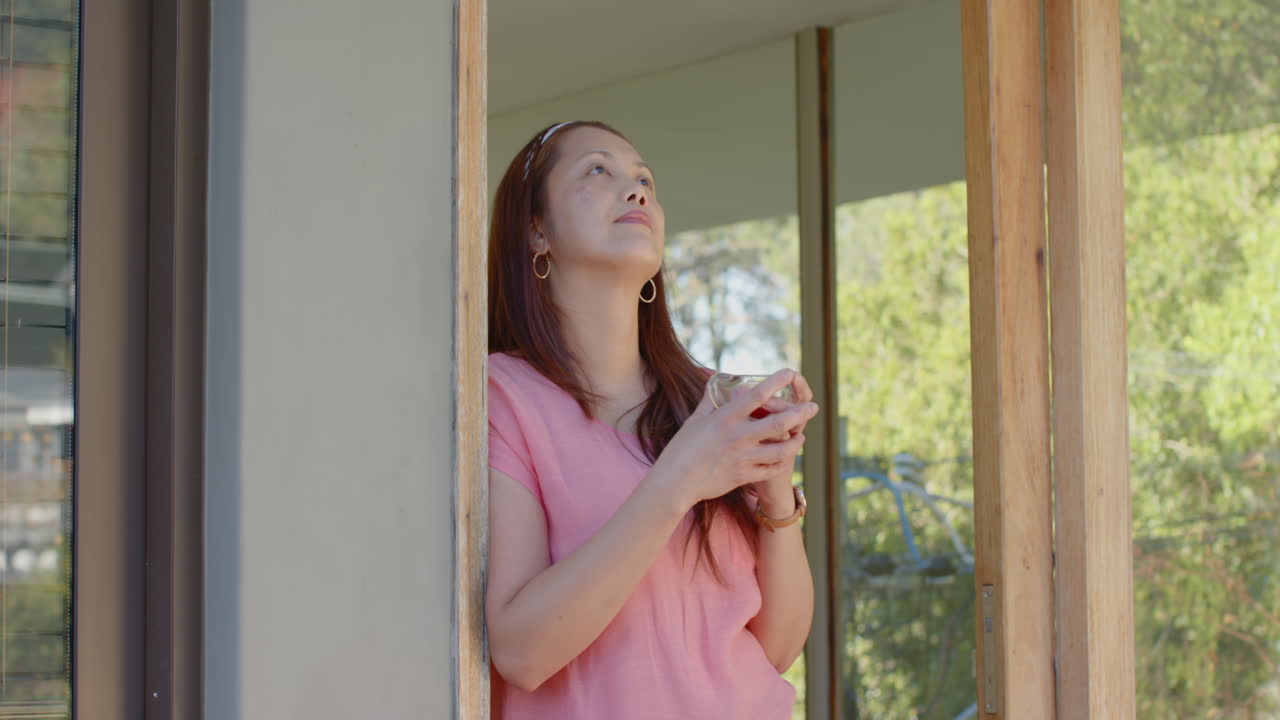 Holding cup, woman standing by doorway and looking outside, enjoying moment