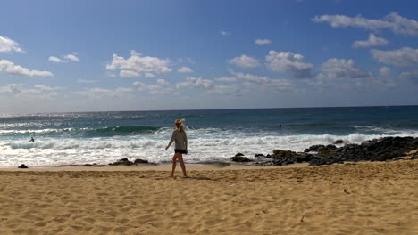 joven rubia camina hacia el mar en la playa del naufragio en la costa sur de kauai, hawaii en el hermoso océano pacífico, 4k