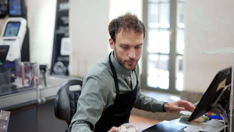 empleado de ventas que trabaja en una tienda de comestibles. un cajero de sexo masculino sonriente con un delantal negro en el mostrador de caja y un cliente irreconocible