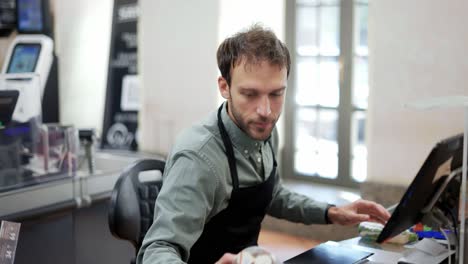 sales clerk working at grocery store. smiling male cashier in black apron at cash desk and unrecognizable customer