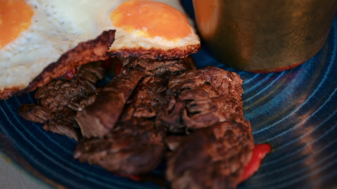 Close up of fried eggs with meat, fries and a dip on a blue plate