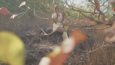 a young beautiful indian girl seen through the dead leaves of a tree painting a clay pot