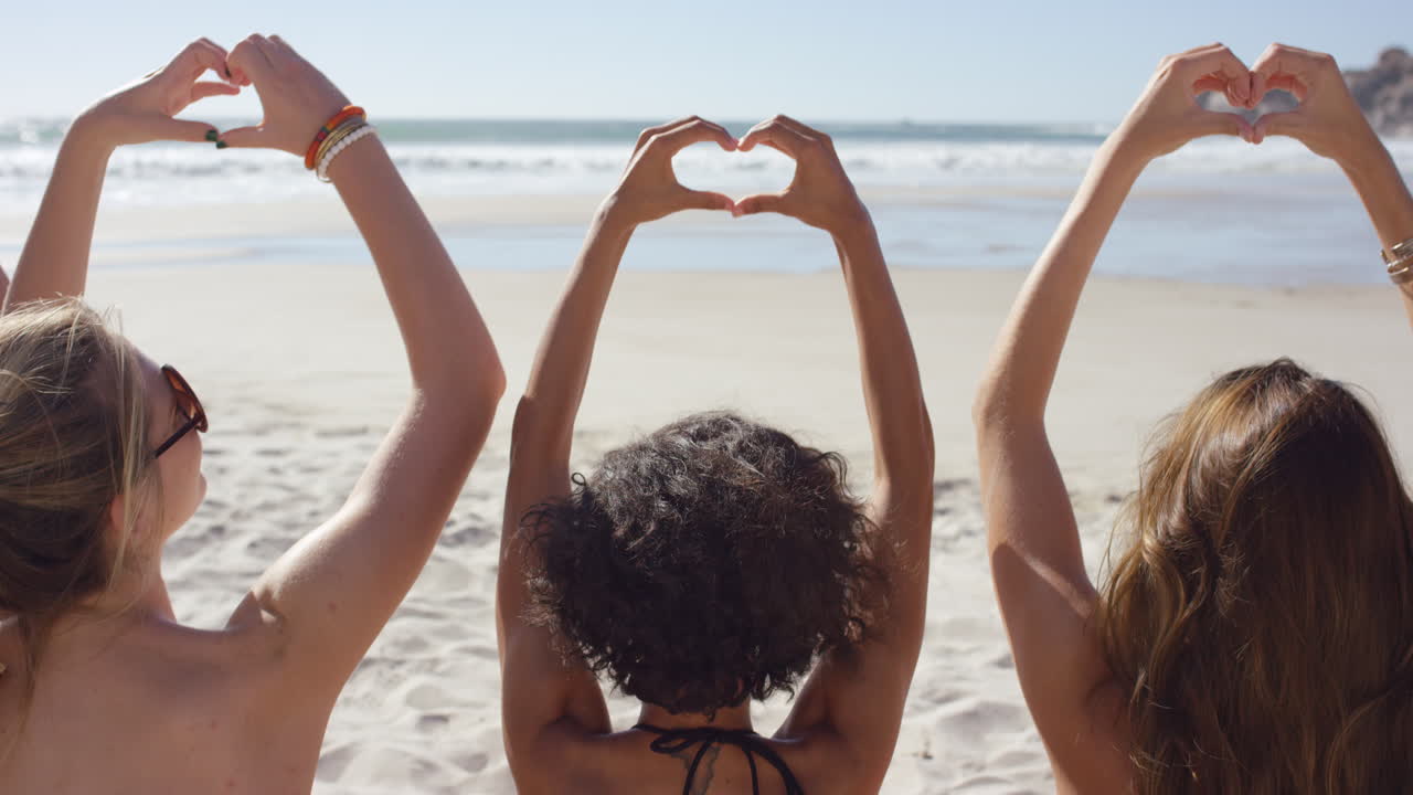 grupo de amigos haciendo un gesto en forma de corazón con sus manos en la playa