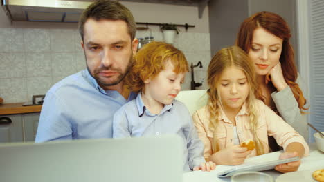 parents and kids eating cookies in the kitchen while they look at something on a laptop