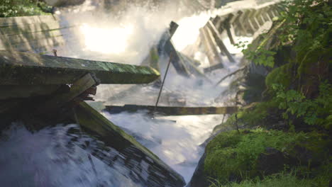 rushing water rapids flowing down log chute and crashing into damaged wooden beams with mossy rocks 4k prores