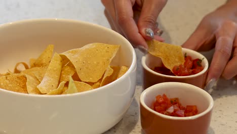 hands adding salsa to chips in a bowl