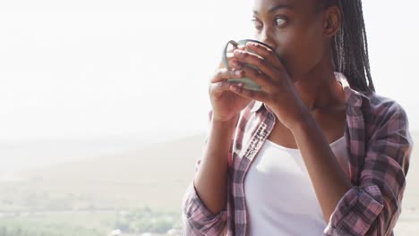 thoughtful african american woman drinking coffee in log cabin, slow motion