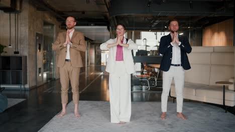 Portrait-of-three-office-workers-who-are-standing-on-the-carpet-doing-meditation-in-the-office-during-a-break.-Harmony-with-yourself-while-working