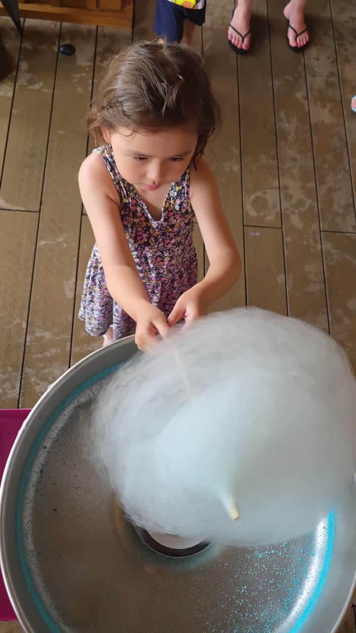 Una bambina di 5 anni osserva attentamente mentre prepara il suo zucchero filato fresco, avvolgendo la dolcezza su un cono a una fiera o un festival - vista dall'alto