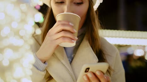 뜨거운 와인을 마시고 전화를 검색하는 여성의 클로즈업 비디오