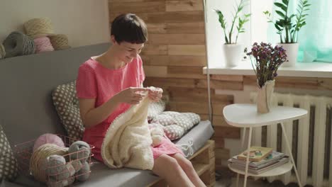 smiling woman on couch and knitting woolen clothes. woman knitting hands