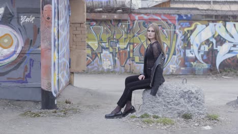 woman in black sitting on a rock by graffiti walls