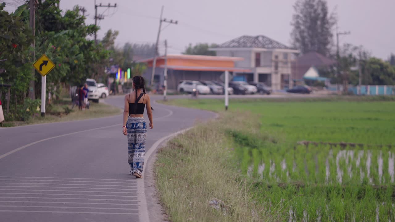 Young woman walking on a rural road next to a green field