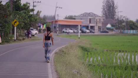 young woman walking on a rural road next to a green field