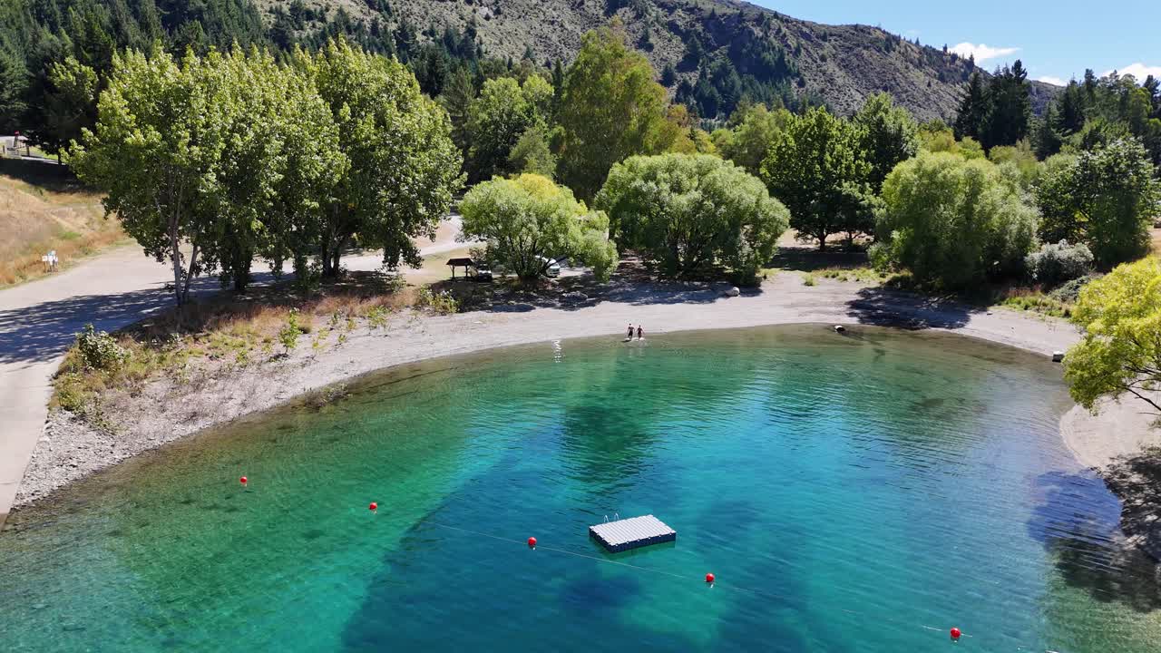 Video 4K di una coppia che esce dal lago Hawea e cammina lungo la costa a Wanaka, Nuova Zelanda. Il lago è circondato da paesaggi naturali, alberi rigogliosi e montagne.