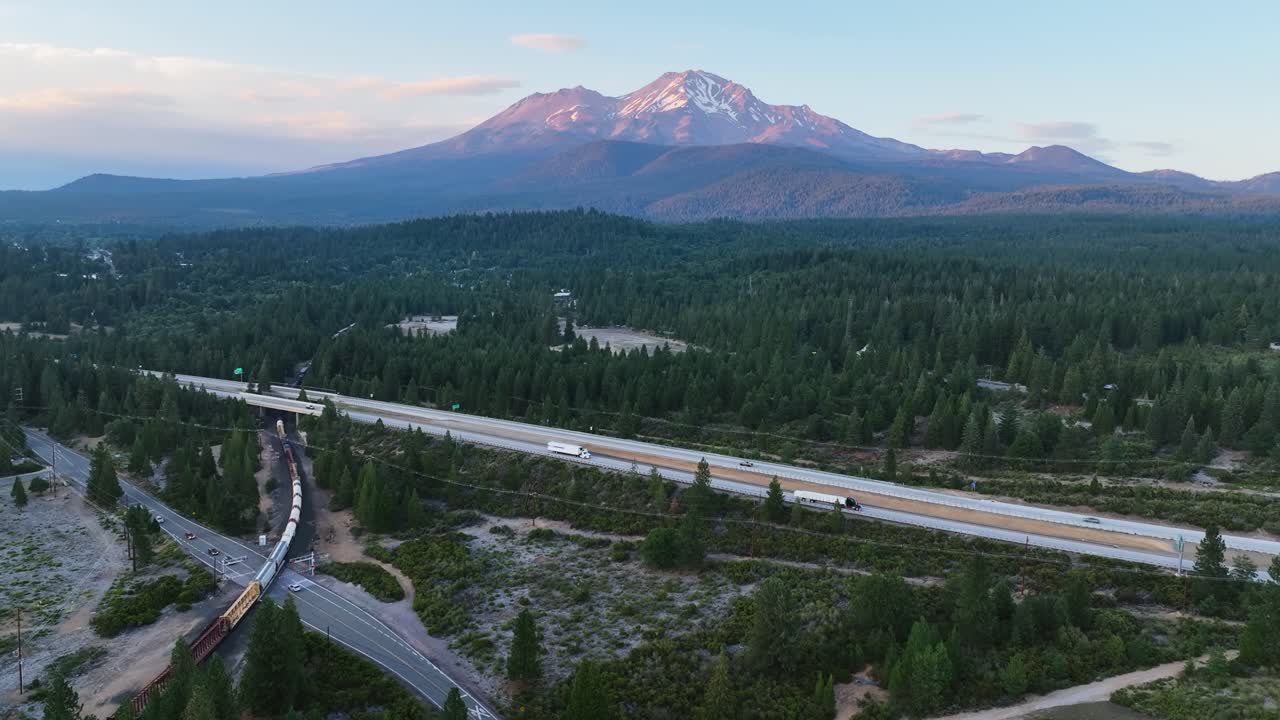 Drone shot of a train and cars with sunlit Shasta Mountain background with snow