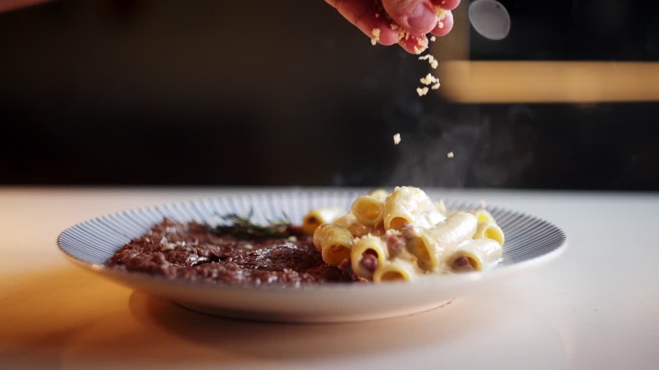 Close up view in slow motion of a Hand spreading grated Parmesan cheese over hot and smoky pasta dish