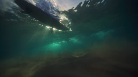 Sparkling-light-across-silhouette-of-long-board-surfers-crossing-as-wave-breaks