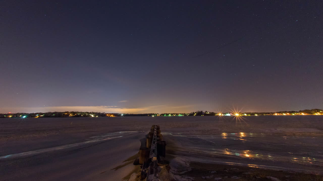 timelapse de las estrellas girando a través del cielo nocturno sobre un río congelado frente a un embarcadero de madera en una noche muy fría