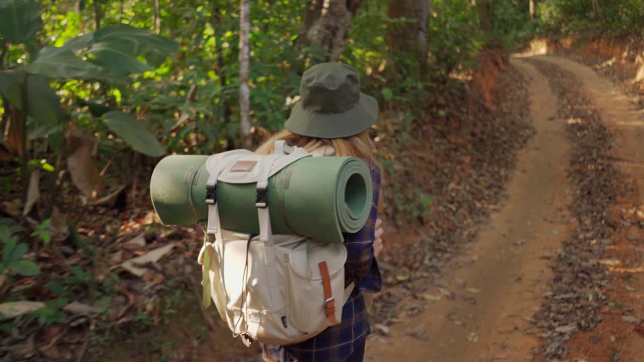 una mujer caminando en la selva de la selva tropical. vista trasera de una excursionista caminando con una mochila a través de la densa naturaleza de la bosque tropical en un día de verano, efecto sol.