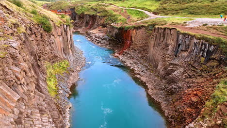 drone flies above the tops of unusual columnar rocks with a river flowing between them. tourists walk and sit on the beautiful boulders.