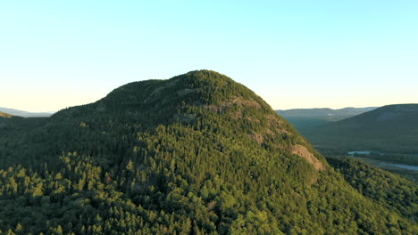 aerial drone shot rising up to the peak of bore mountain over thick green forest trees and lakes of the maine wilderness